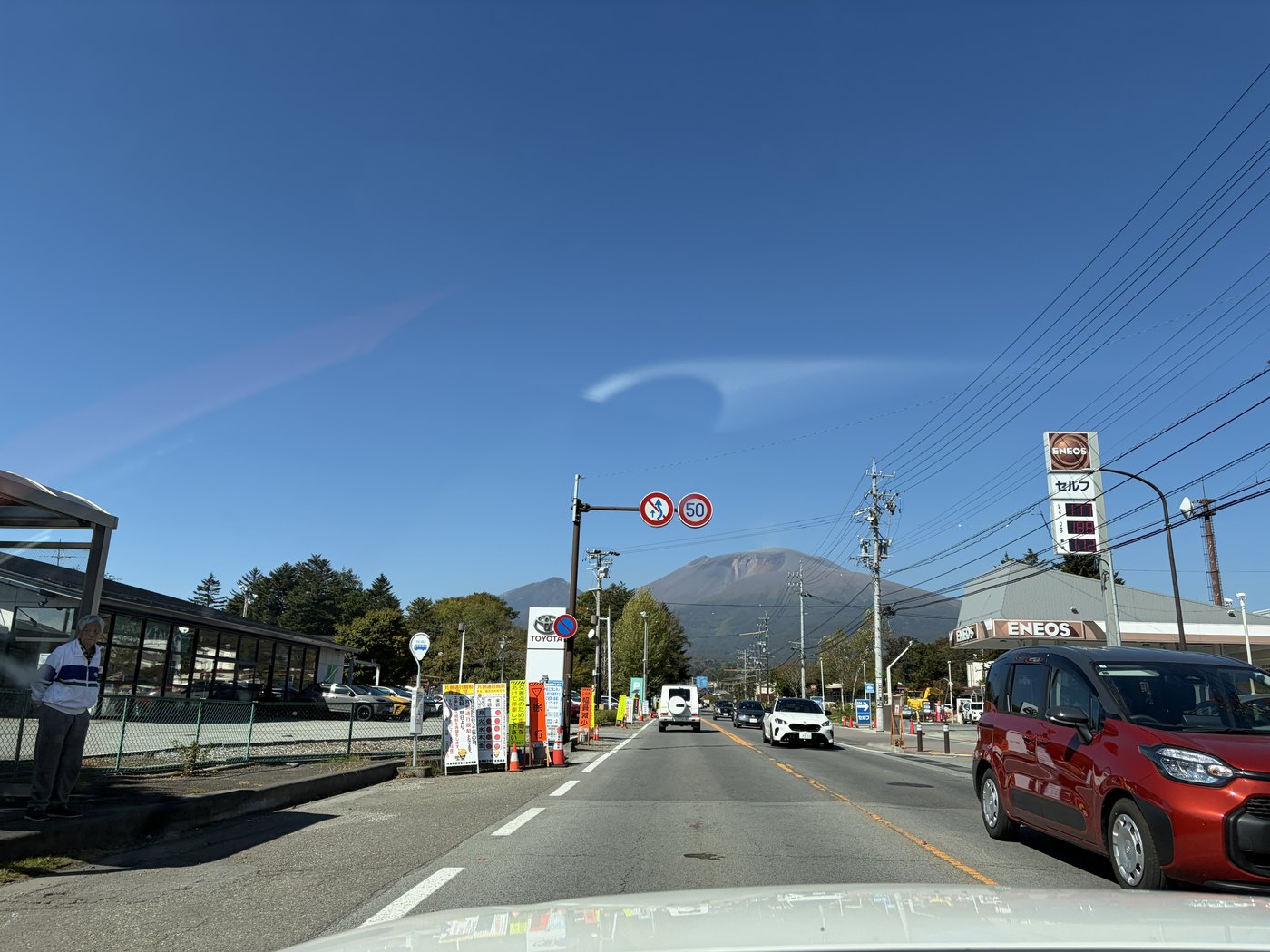 雲の少ない青空の下、道路の先に見える浅間山