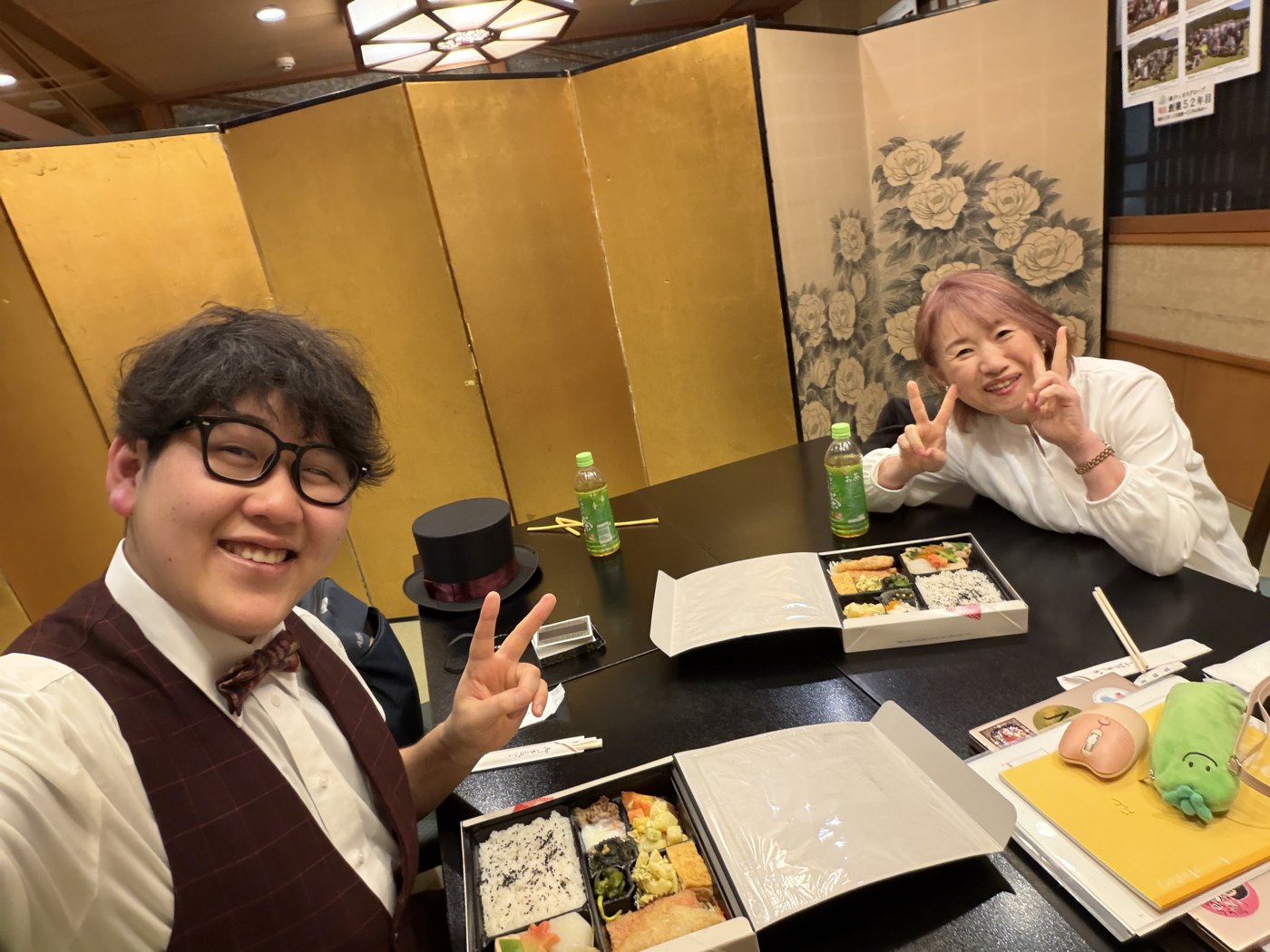 金屏風のある個室で、お弁当を前にピースをするDaiSuke