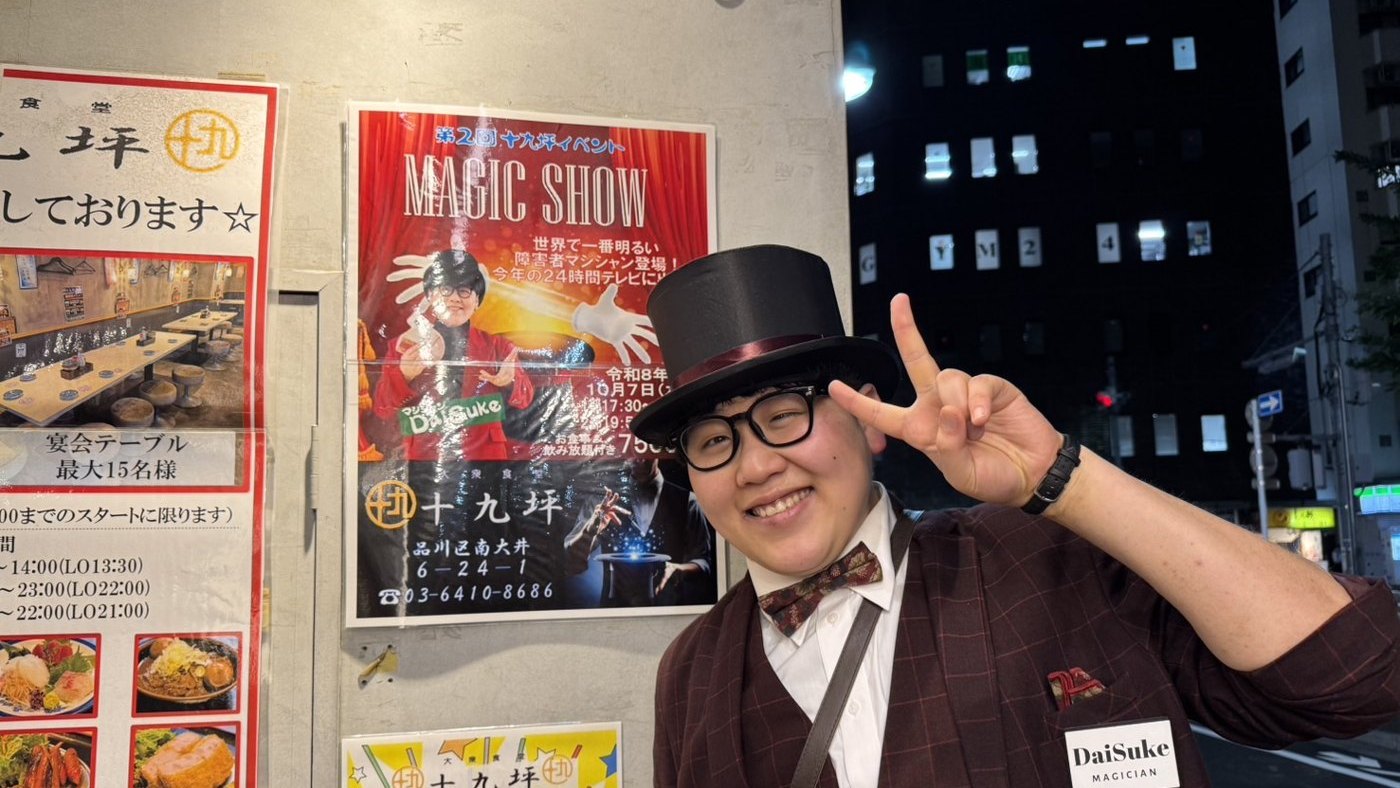 大衆食堂 十九坪の店頭に貼られたMAGIC SHOWのポスターの横で、シルクハット姿でピースをするDaiSuke