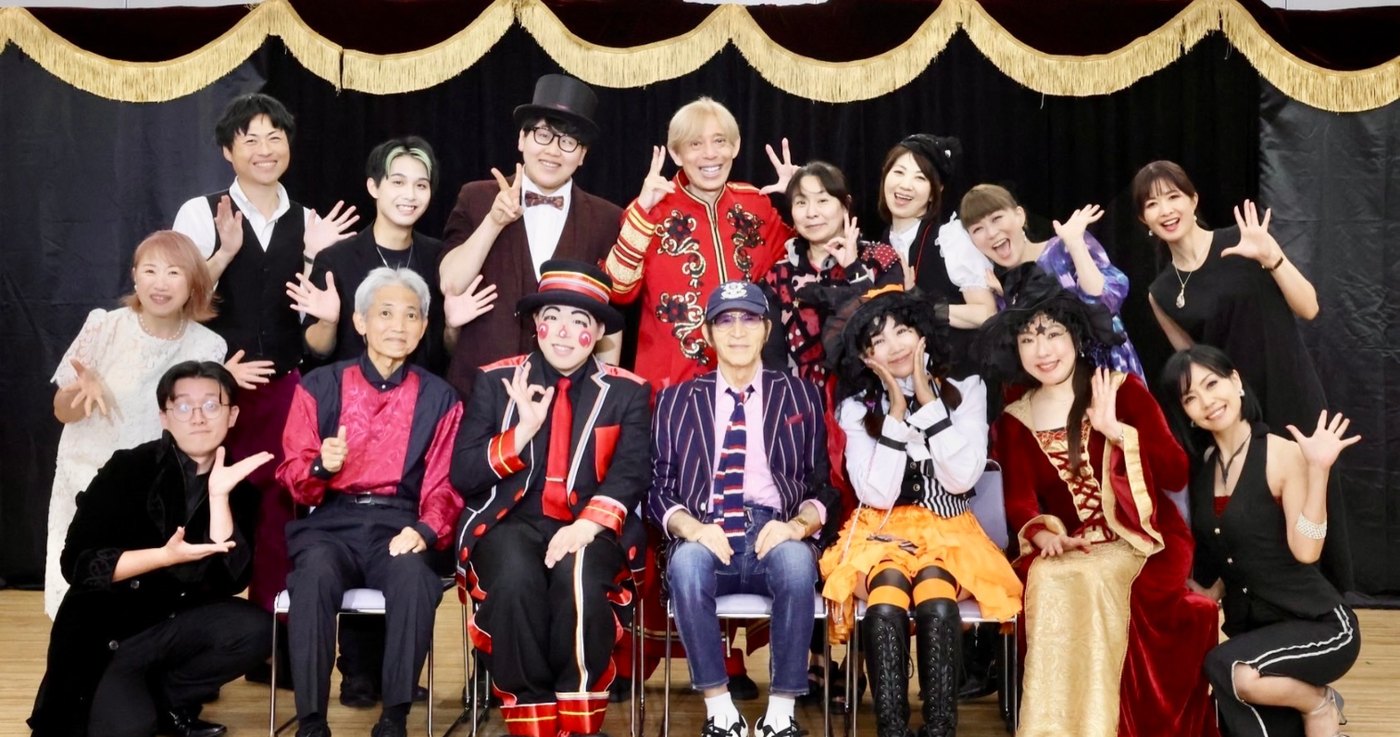 金色のフリンジが付いたステージ幕の前で、プリあらの出演者の皆さんと並ぶDaiSukeの集合写真