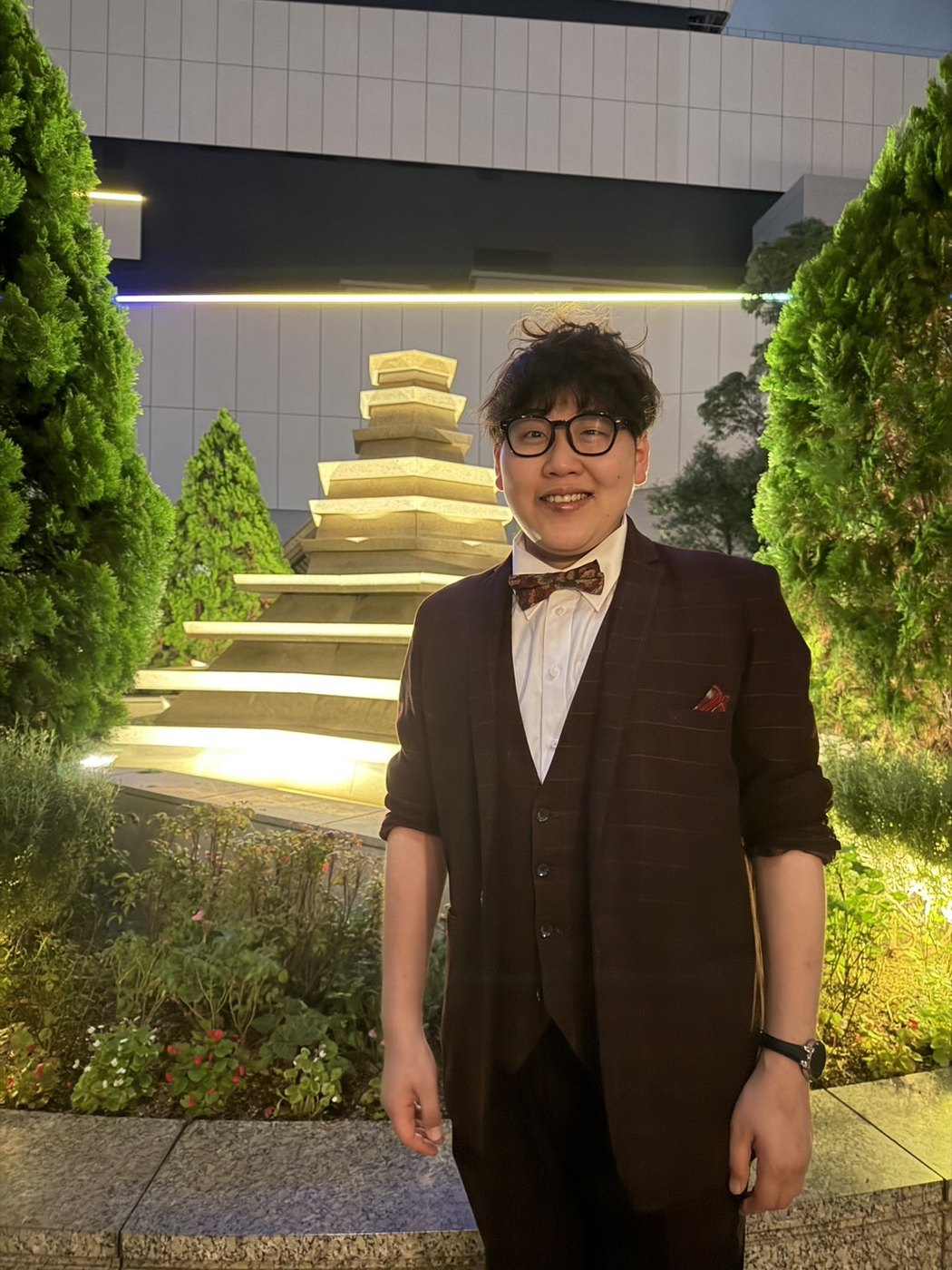 ライトアップされた夜のホテル外構の植栽の前に立つDaiSuke