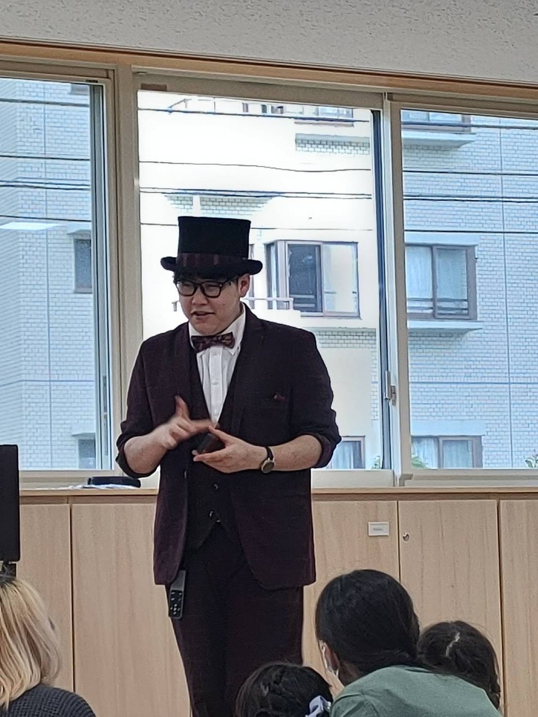 シルクハットに蝶ネクタイ姿のDaiSukeが、手元のマジックを子どもたちとご家族に見せている様子